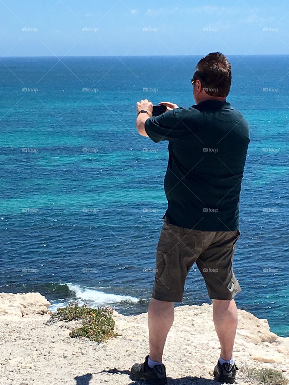 Man on bluff taking smartphone photo of ocean