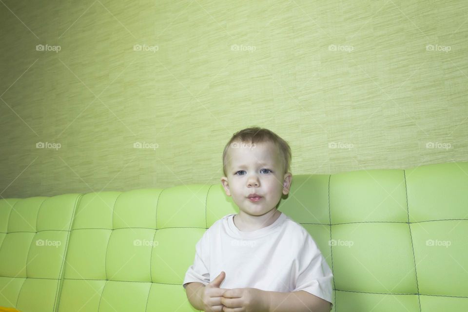 A portrait of a child sitting at home on a green sofa depicts different emotions in yellow shorts.
