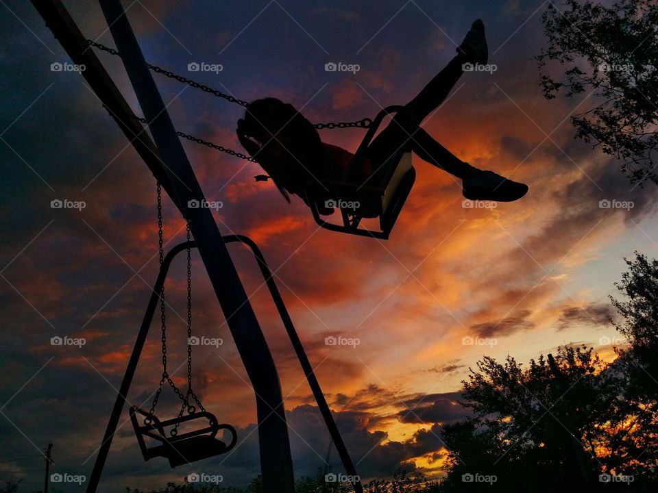 Swinging girl on sunset background