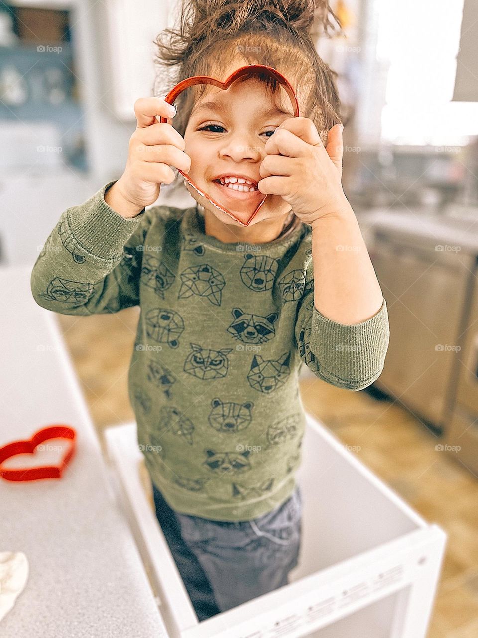 Cute toddler holding heart cookie cutter, toddler making heart shaped cookies, baking with toddlers, winter time activities, staying indoors with toddlers, heart shaped face, cute toddler in the kitchen, little girl helps mommy bake valentines treats