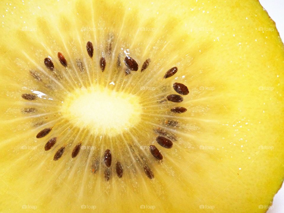A macro shot of a cut golden kiwi, showing its yellow flesh and seeds.
