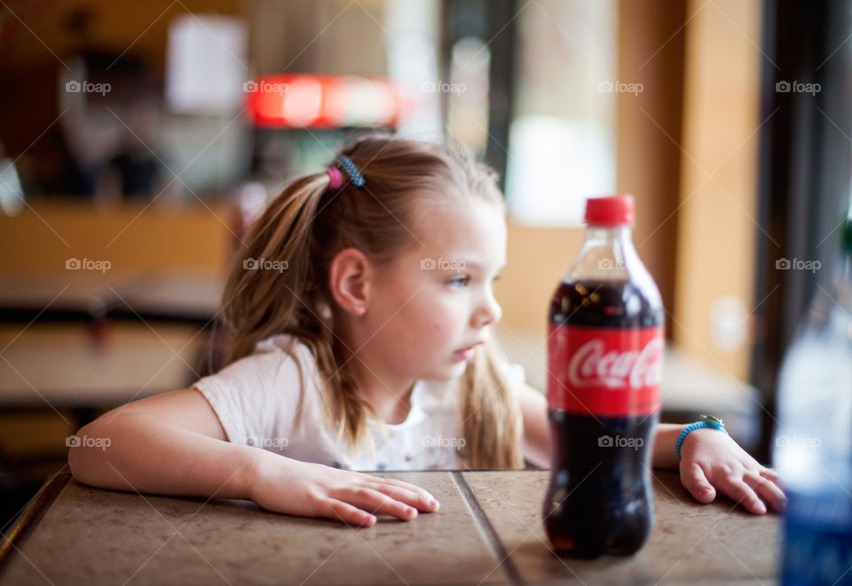 Cute little blonde girl with serious expression, sitting with a Coke while she patiently waits for her pizza. 