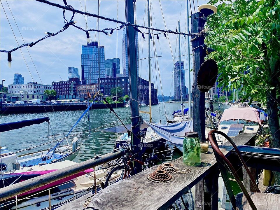 On the tree lined narrow shore the boat people here at “Newtown Creek” in LIC, Queens have built a nice wooden veranda that is sometimes used for parties and special get togethers. 2023. Hypnotic Productions