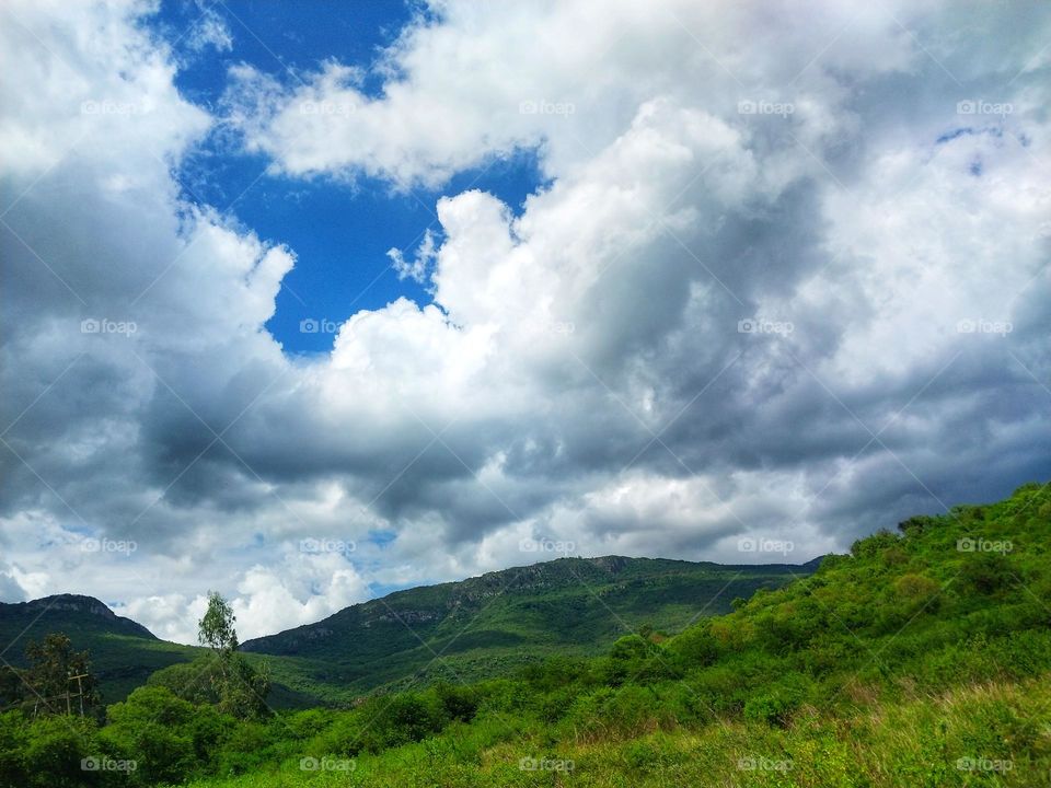 clouds rolling in over a green field and mountain top