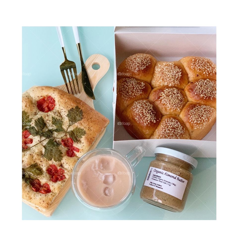 Wholesome healthy treats consisting of foccacia , heart shaped tomato cheese buns, almond butter for afternoon tea snack in flatlay 