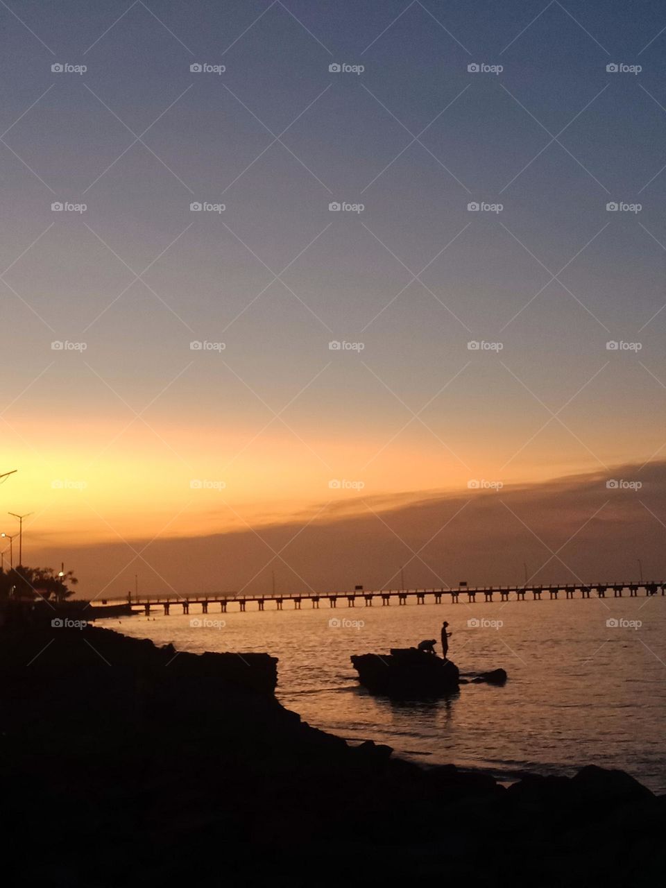 Fishing during sunset at Praia dos Coqueiros in Dili. Rock in the water