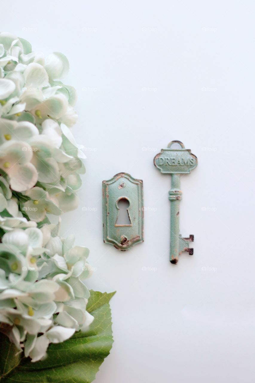 Overhead view of light teal, vintage, metal key with embossed word, “Dreams,” and keyhole with light teal hydrangeas on white background - 