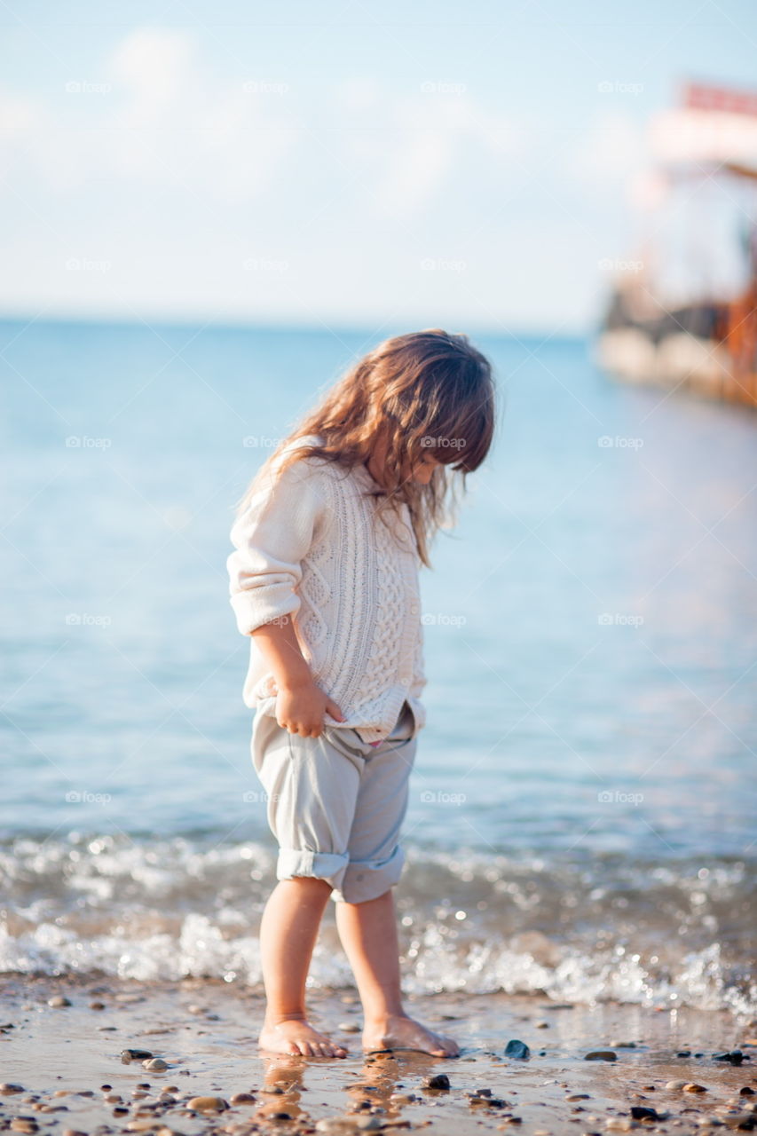 Little girl walking on the sea shore at sunny morning 