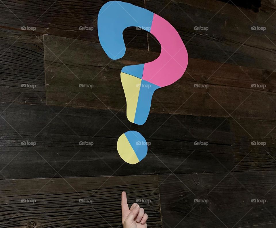 QUESTION MARK Lettering Made Of Geometrical Shapes With Pink, blue And Yellow. Questioning And Wondering What Is Going On With Finger Pointing Up At The Question Mark, Showing.