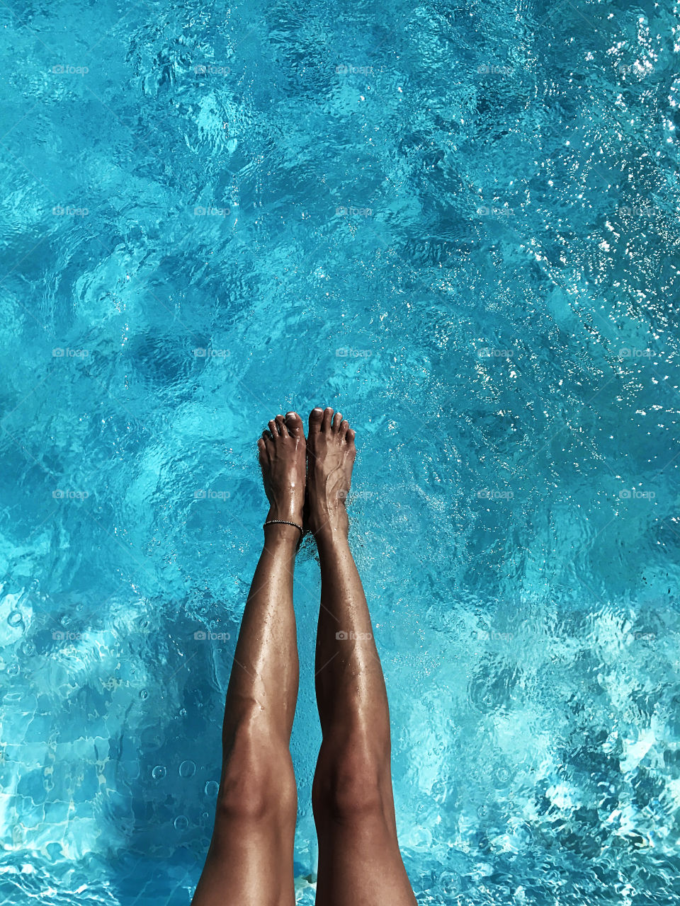 Female feet over the blue water in the swimming pool 