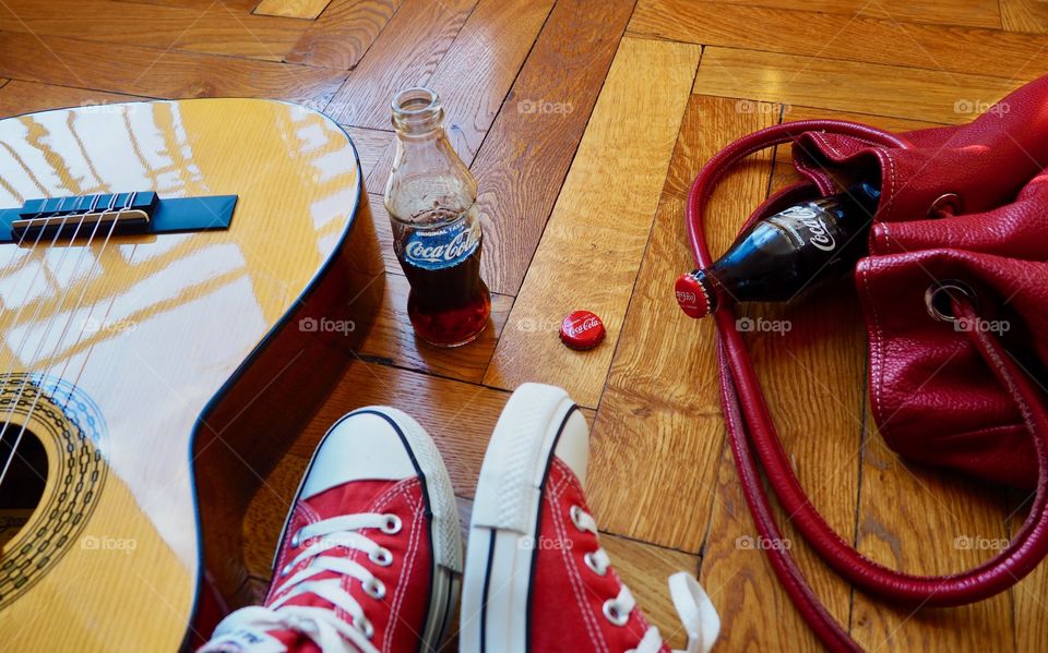 Coca Cola bottles on hardwood floor with red sneakers and red leather bag.