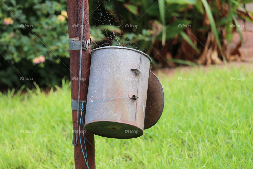 Rusty old tin clothespin clothes peg tin container attached to rusty iron pole in backyard outdoors