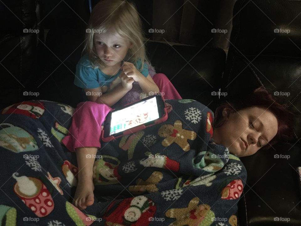 Toddler sitting on older sleeping older sister while playing on iPad 