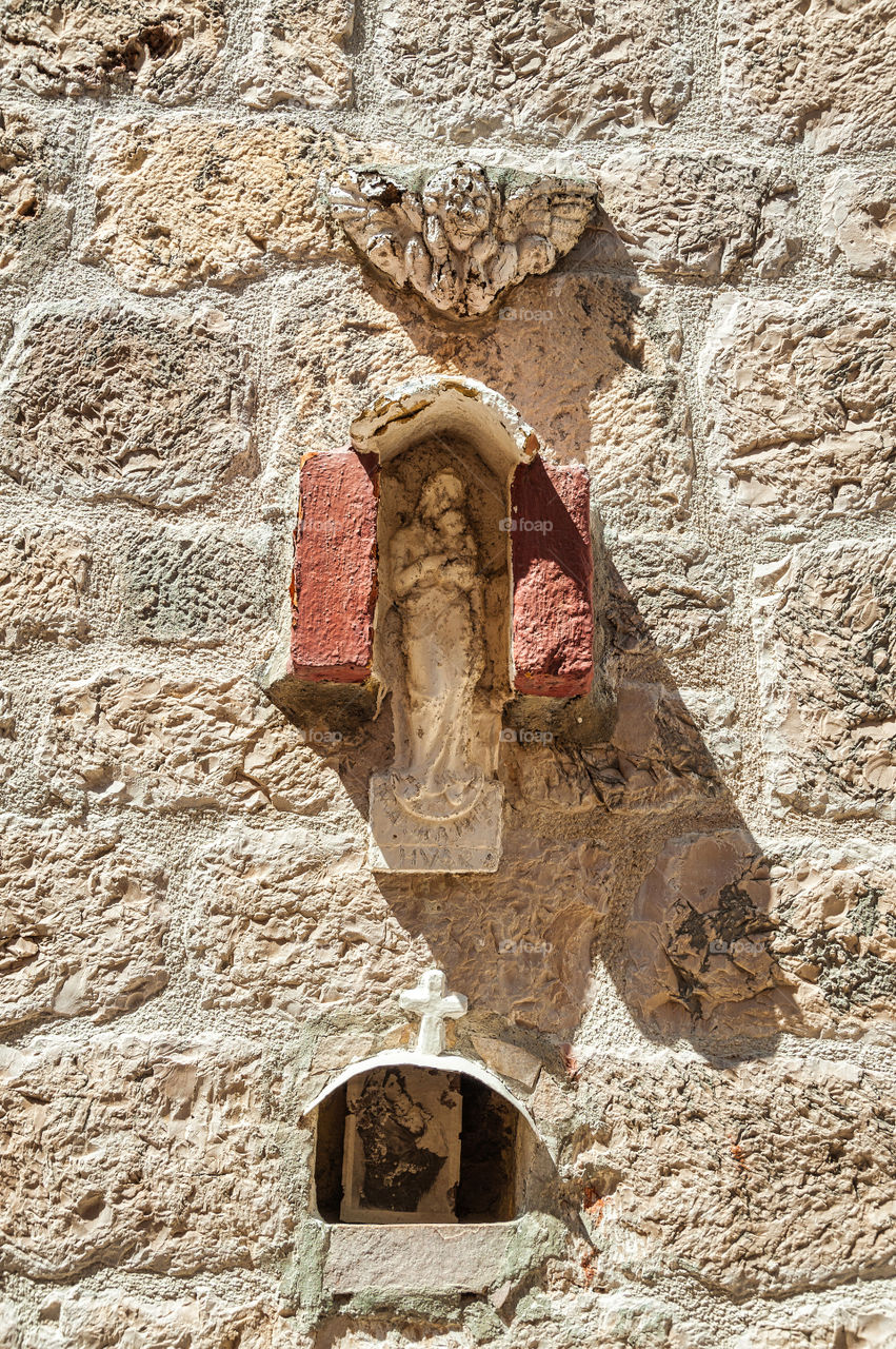 An Angel, Virgin Mary with a Child, a Cross. Three important symbols, figures of Christianity carved into stone wall.