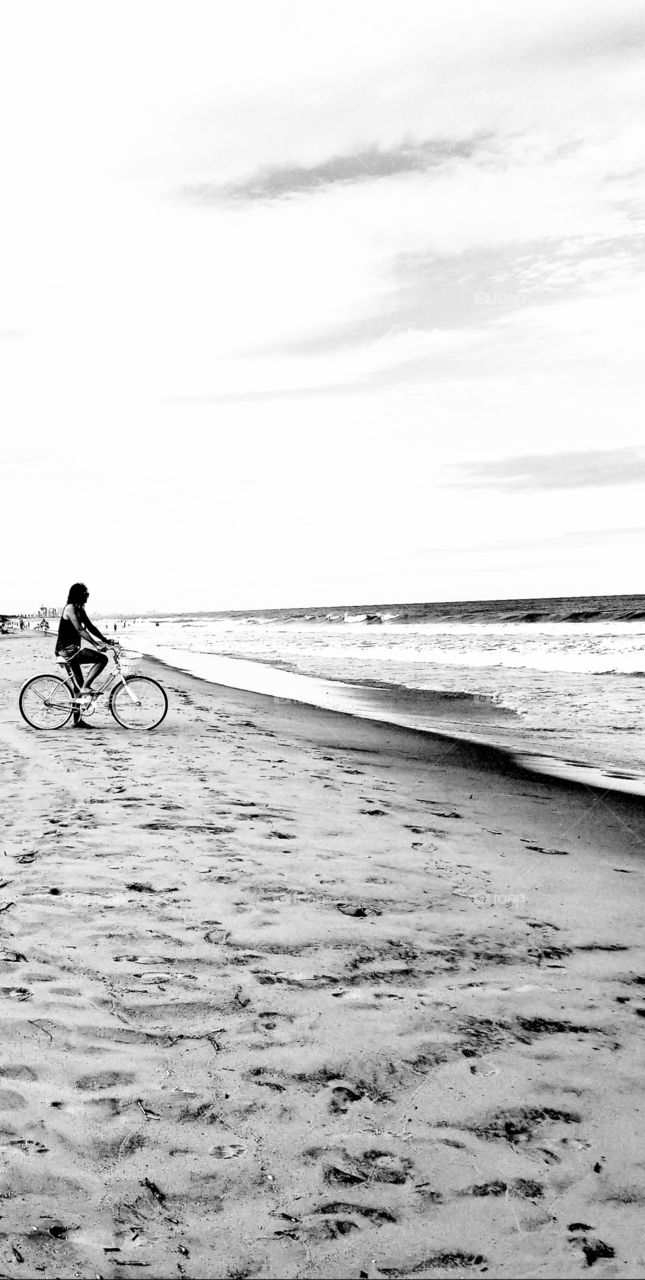 Woman on a bike on the beach and looking out at the ocean