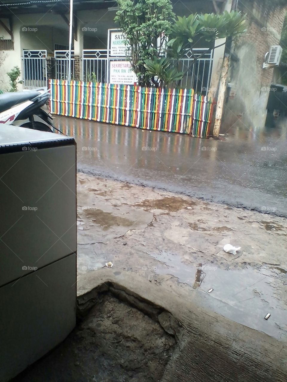 A colorful fence in a village office on the roadside that is wet with rain