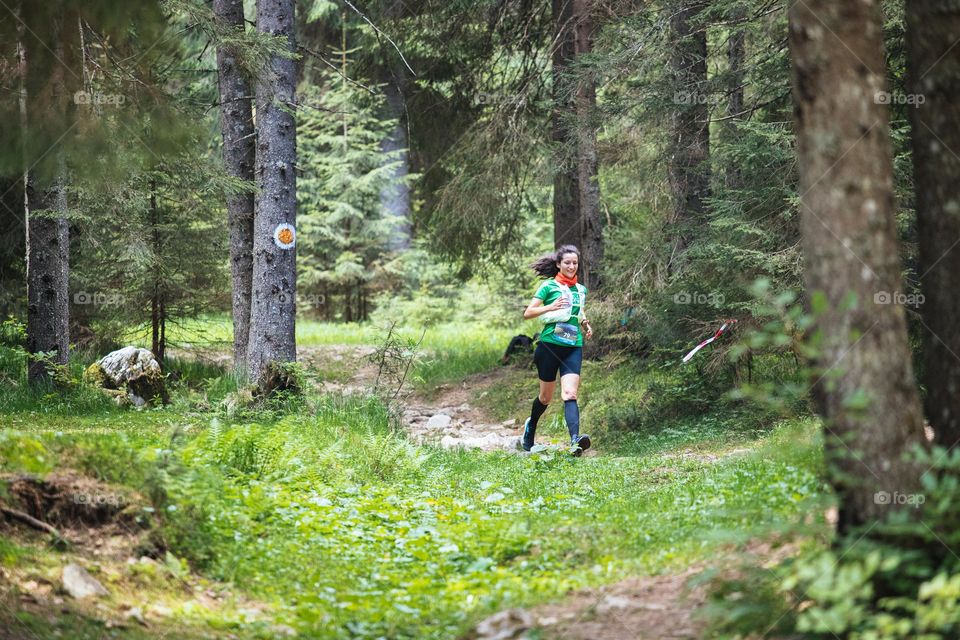 Woman dressed in a green t-shirt and black shorts, running at a trail-run competition in the forest.