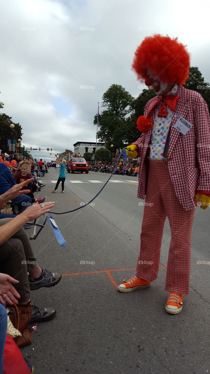 A clown entertaining people with his invisible dog during a parade.