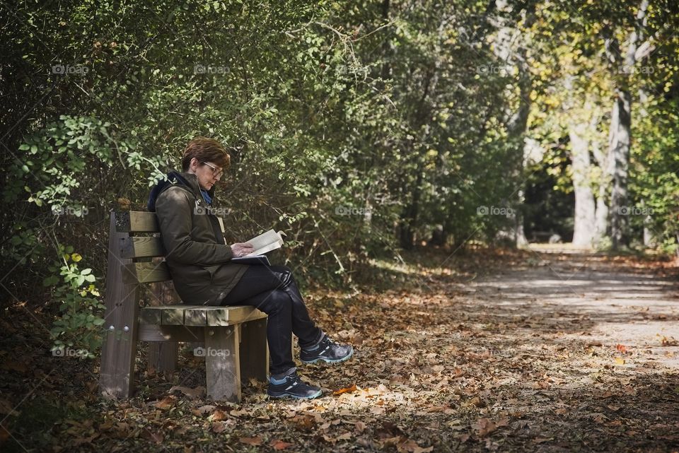 A woman reads a book sitting on a bench