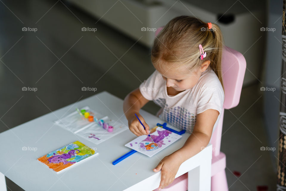 Cute little girl with blonde hair drawing at home 
