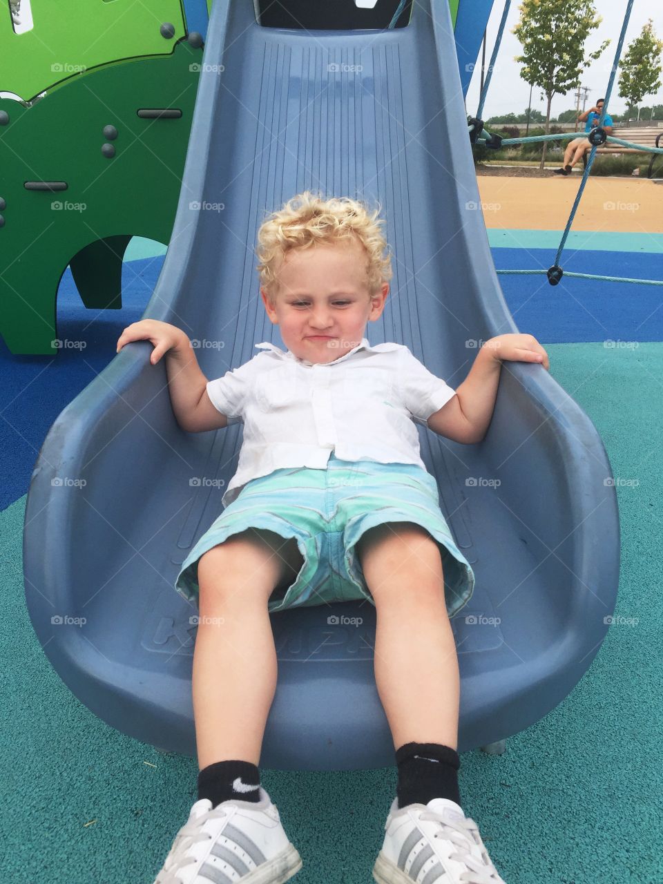 Toddler boy going down the slide at a playground 