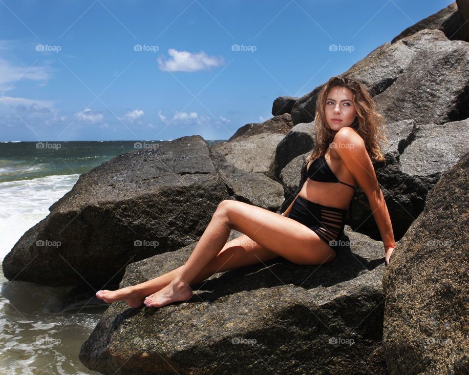 Sensual young woman posing on rock at coastline