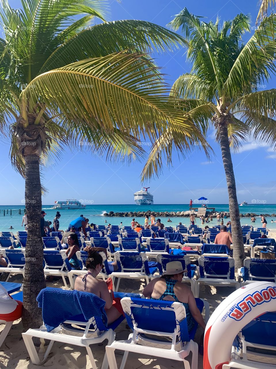 People sunbathing on lawn chairs on the beach with the crew ship in the background