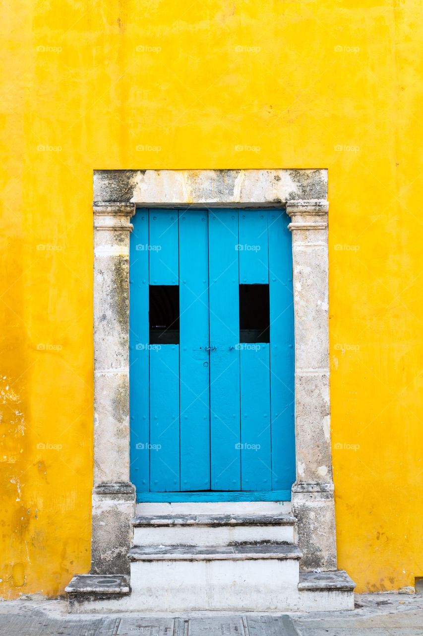 Blue door on yellow building. Bright blue double door in brightly yellow painted building. Strong color contrast. Grey Stone stairs. Closed doors. Colorful