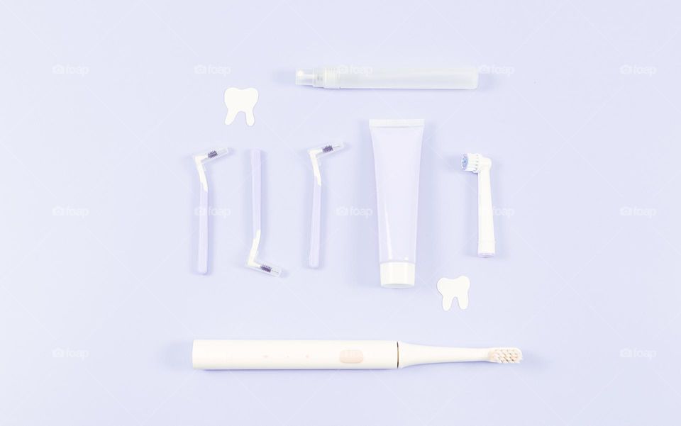 A set of toothbrushes, oral perfume and toothpaste lie in the center on a delicate lavender background, flat lay close-up. The concept of personal hygiene