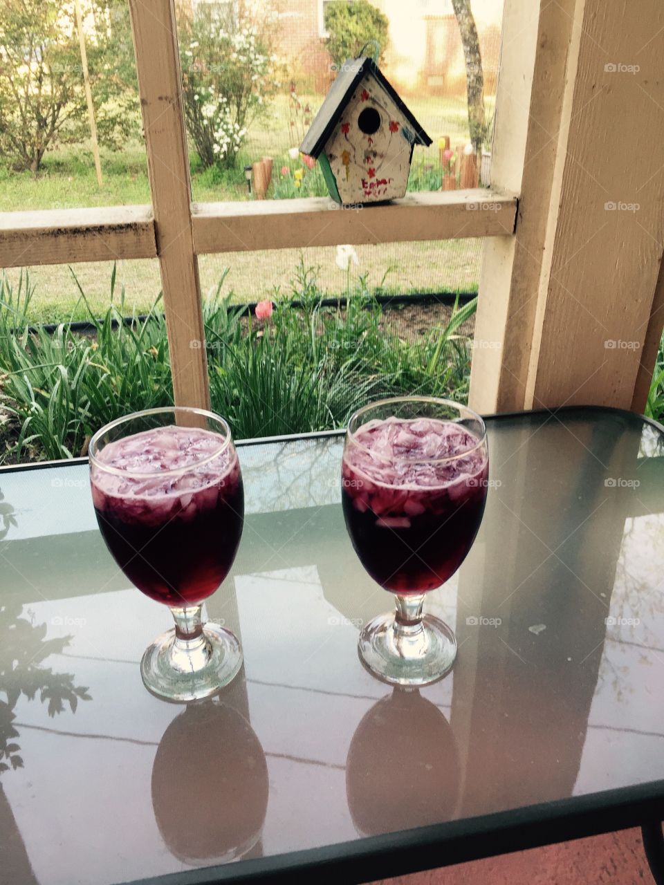 Two glasses on glass table on the pitch with wine in them.