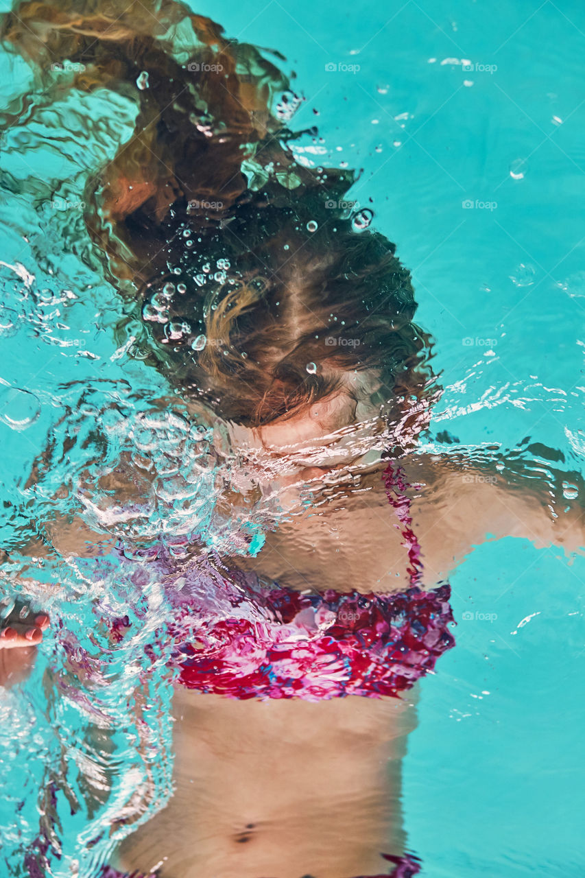 Young woman immersing herself in water, practicing, learning to swim in pool. Candid people, real moments, authentic situations