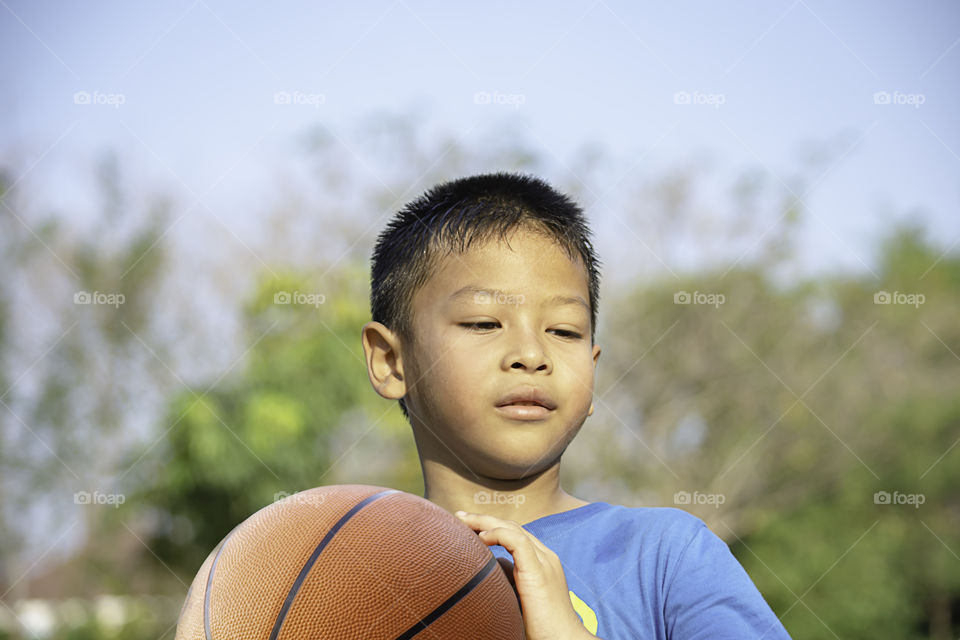 Asian boy holding a basketball ball Background blurry trees.