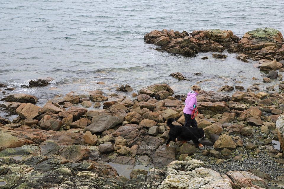 Woman walking her dog on a rocky shore 