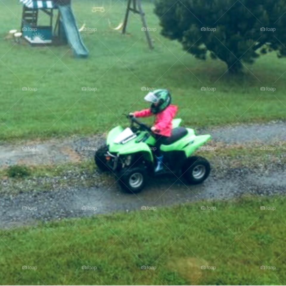 Little girl dressed in pink driving her green four wheeler outdoors. Going on an adventure!