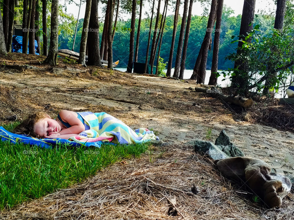 Little girl naps on lake shore during the summer.