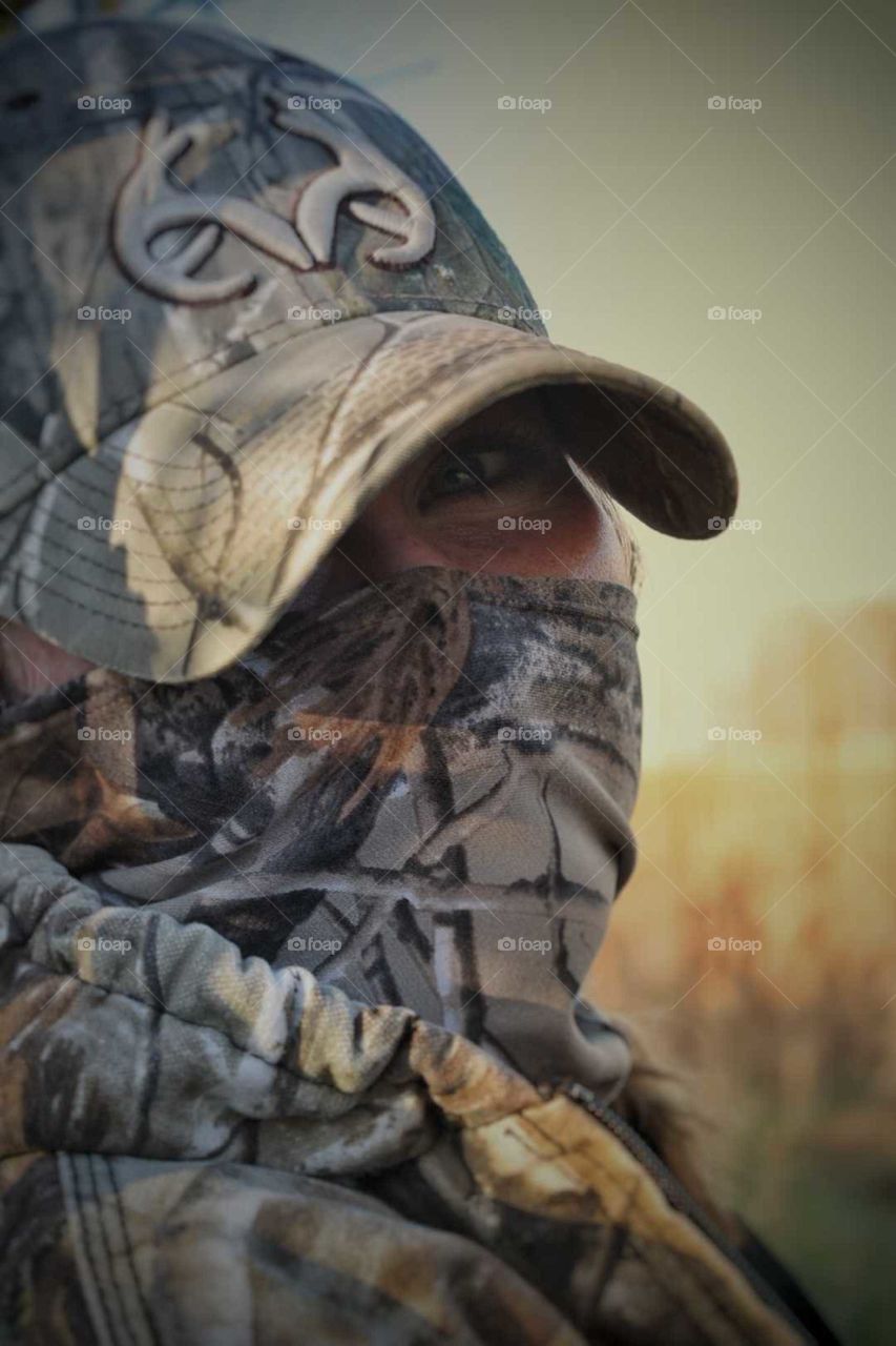 The glistening eye of a female hunter, fully concealed in camo in the warm and glowing sun.