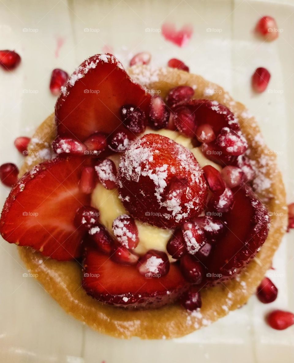 Home made delicious and yummy strawberry tartlet with vanilla pastry cream decorated with red pomegranate seeds and powder sugar from above 