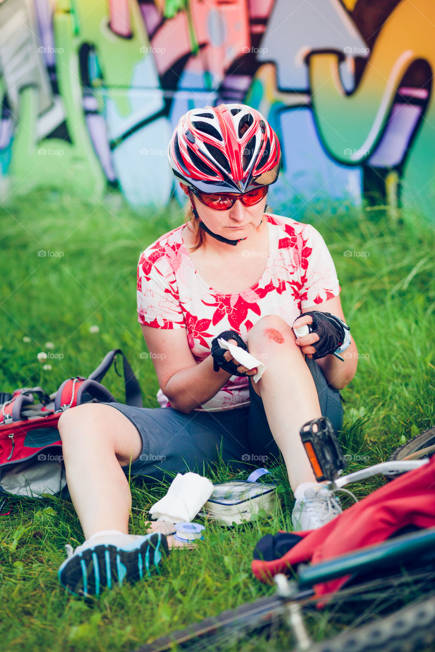 Woman dressing the wound on her knee with medicine in spray and gauze on bike trip on summer day