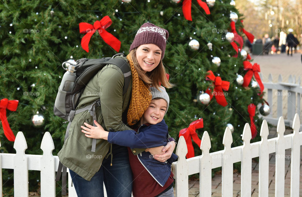 Mother and son hugging in front of a decorated Christmas tree outdoors