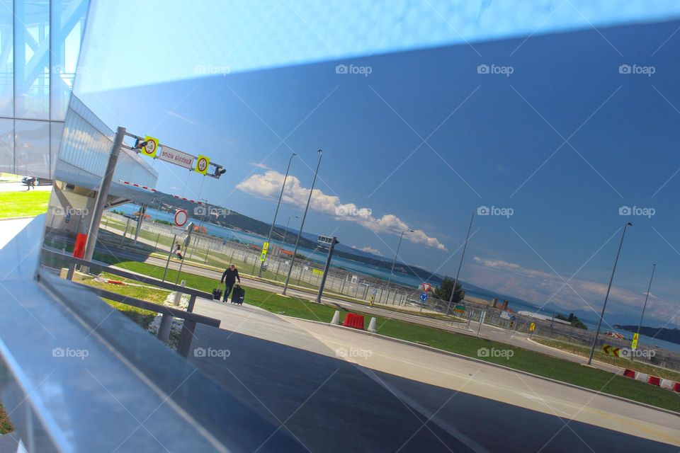 Reflection in the glass of the airport building.  A passenger with suitcases goes to the airport Split. Croatia