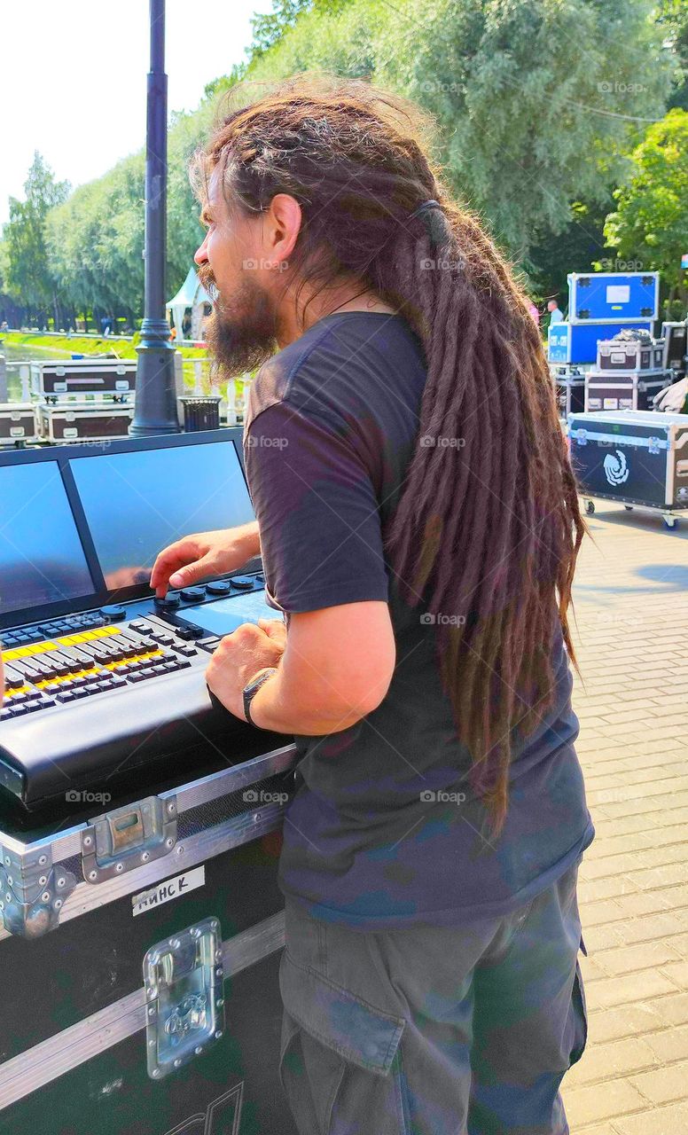 A man stands behind a sound concert equipment. On the head of a man, a hairstyle of long dreadlocks, which are gathered in a bun