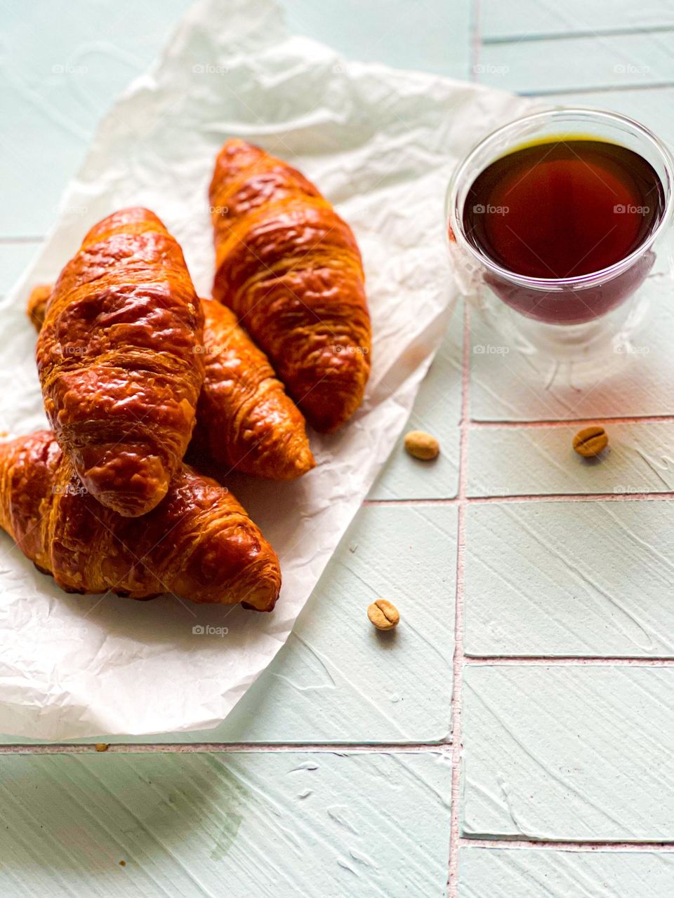 Croissants and a cup of hot black coffee. Close up view and coffee beans scattered at the side