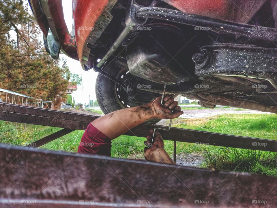 car repair on a flyover without a lift. in the frame, the hands of the master in oil hold a wrench.