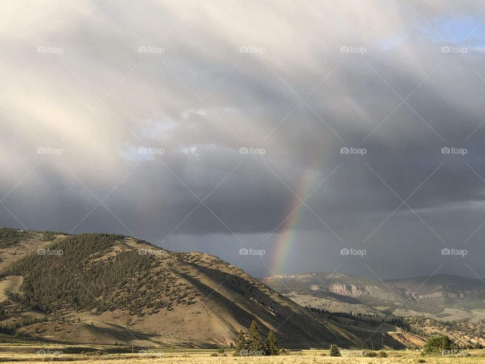 Rainbow breaking through the clouds with mountain backdrop.