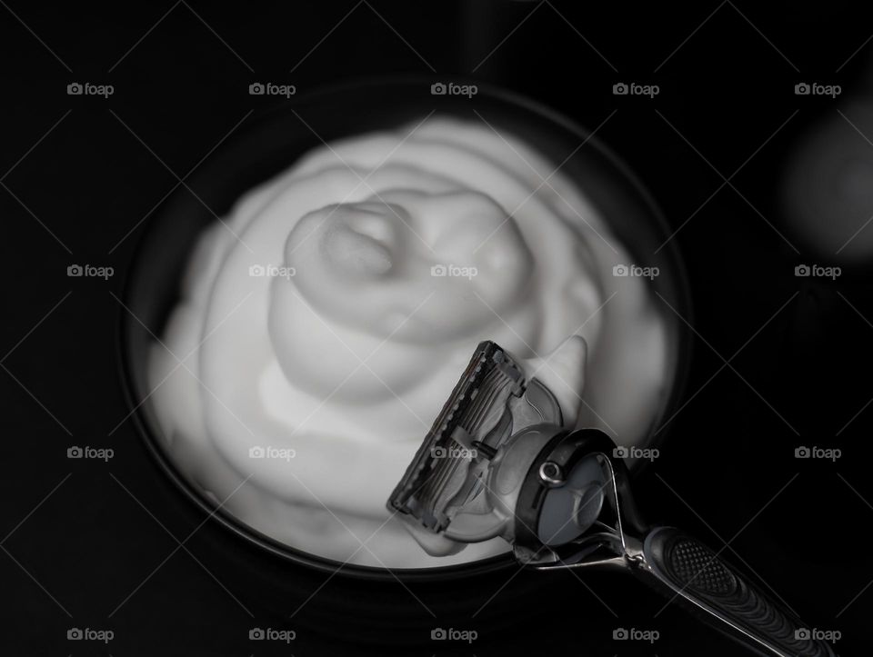 Razor for shaving beard on the edge of the porcelain bowl with shaving foam stand on a black background,side view. The concept of a barbershop man, shaving man, beard care.