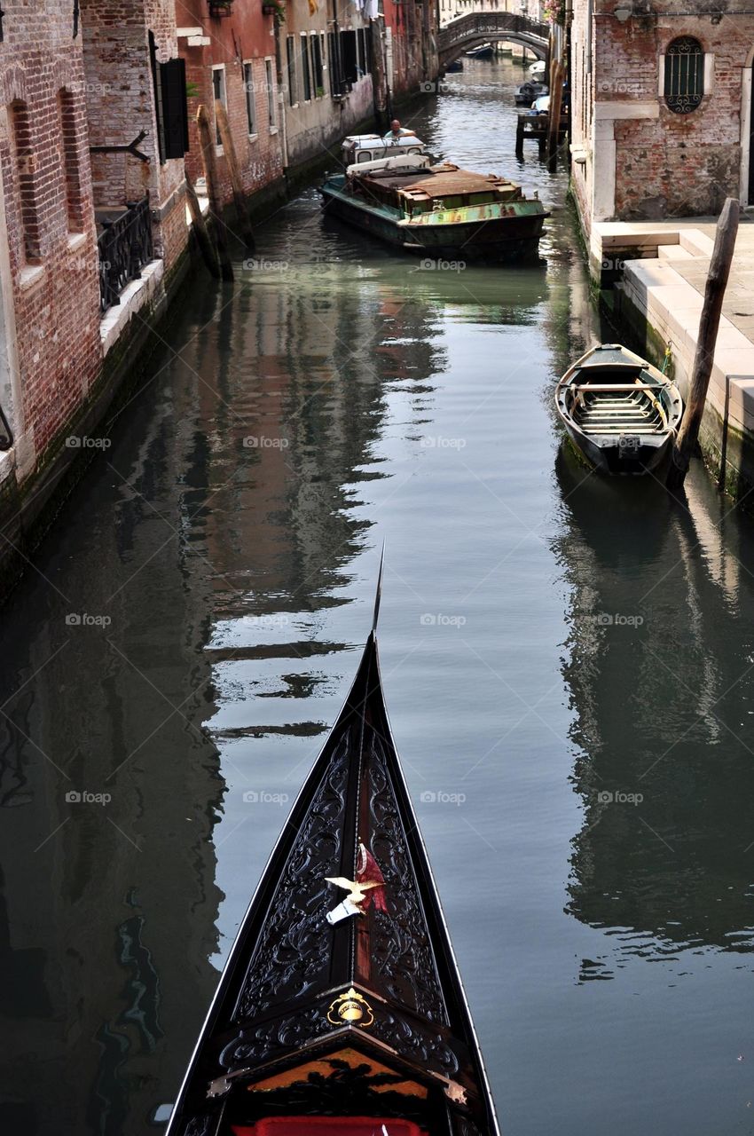 Iron prow of a gondola crosses the waters of a canal in venice