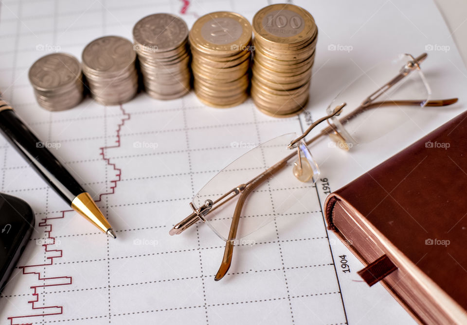 монеты ручка очки и смартфон на финансовом графике