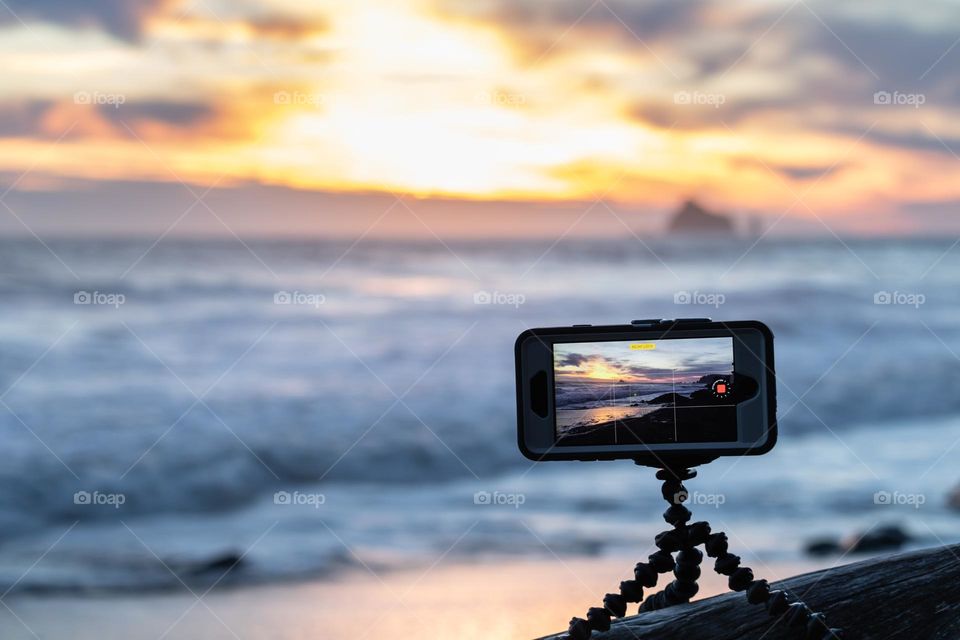 An iPhone set up on a mini tripod capturing a beautiful sunset on a beach.