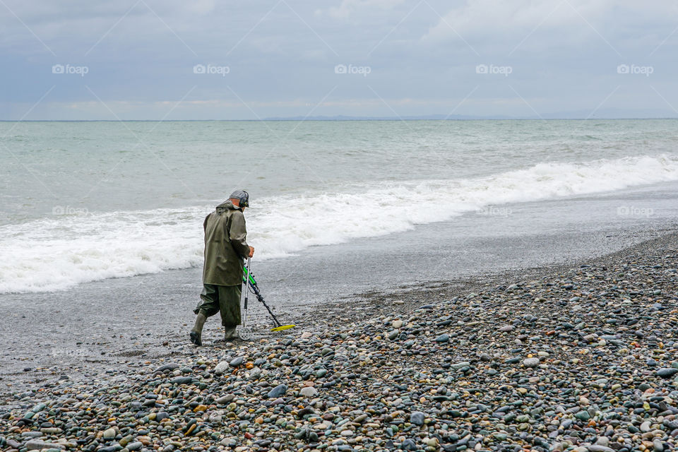 a man with a metal detector walks along the beach, treasure hunter