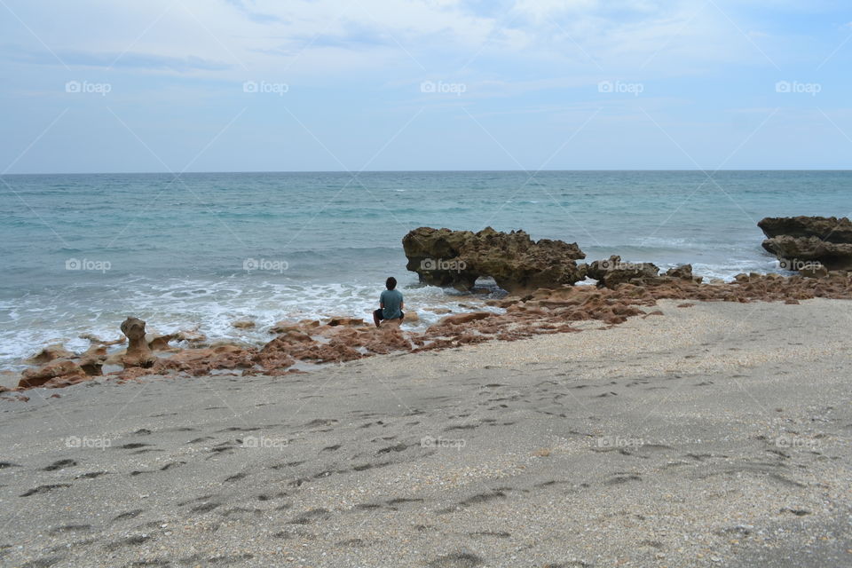 Rear view of man sitting on rock at beach